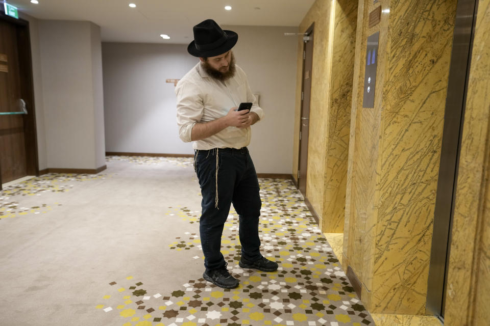 Eli Chitrik from Turkey checks his phone as he waits for lift at his hotel in Doha, Qatar, Monday, Nov. 28, 2022. Stored into bright orange cases in Rabbi Eli Chitrik’s hotel room are bagels stuffed with vegetables. The labels declare the sandwiches kosher, or in compliance with Judaism’s set of dietary regulations. Freshly baked, they are made in Qatar at a designated kitchen, set up to feed Jewish World Cup visitors who want to keep kosher during the tournament. (AP Photo/Moises Castillo)