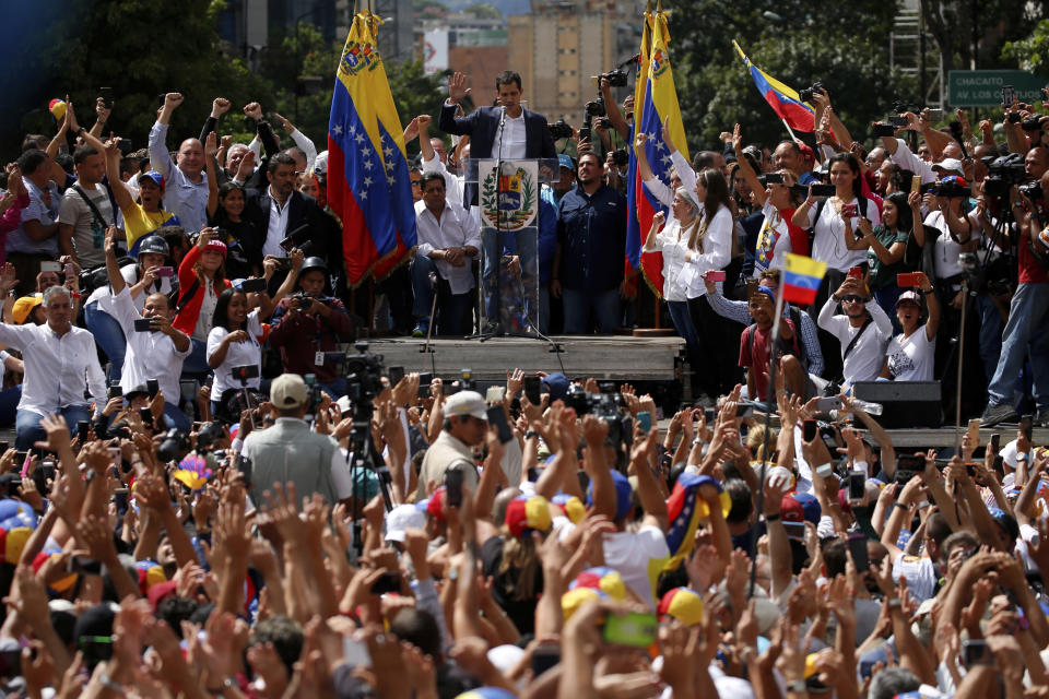 Juan Guaido, head of the opposition-run congress, looks down and holds up his hand during his symbolic swearing-in as interim president of Venezuela on a stage during a rally demanding President Nicolas Maduro's resignation in Caracas, Venezuela, Wednesday, Jan. 23, 2019. Guaido declared himself interim president. (AP Photo/Fernando Llano)