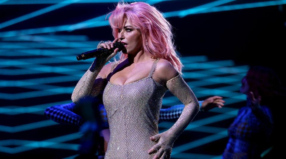 Shania Twain with pink hair in a sparkly jumpsuit on stage sings at the Peoples Choice Awards