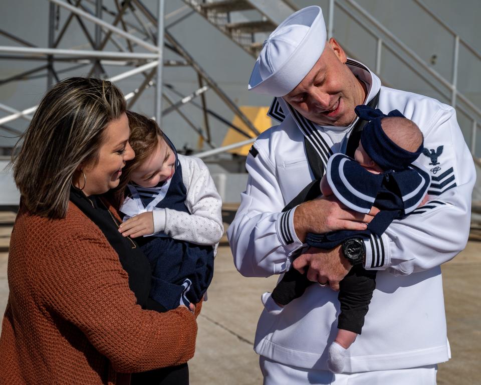 Corey Mink (right) holds 3-month-old daughter Charlotte for the first time as wife Julie and daughter Olivia, 4, welcome him home in time for the holidays.