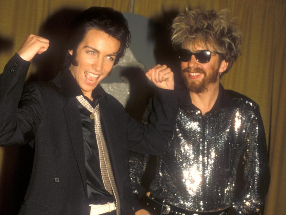 Annie in an Elvis-like wig and a black suit and tie making a muscles pose and Dave smiling in sunglasses and a shiny silver jacket.