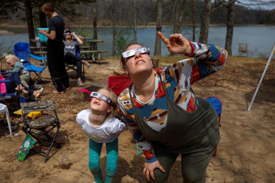 Brittany Sunderman and Gianna Debenham, 6, from Effingham, Illinois, and other members of the Debenham family who traveled from Utah and Las Vegas to experience the total solar eclipse together, try out their eclipse viewing glasses at their campsite a day ahead of the event at Camp Carew in Makanda, Illinois, U.S., April 7, 2024. REUTERS