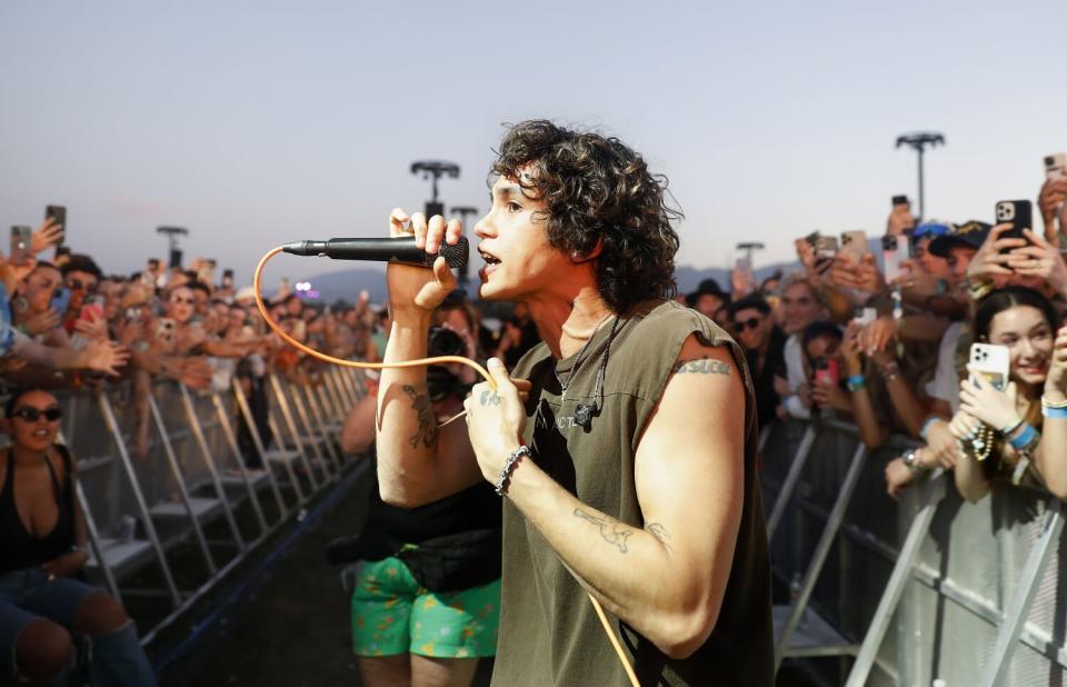 A young man sings into a microphone, surrounded by people behind barricades