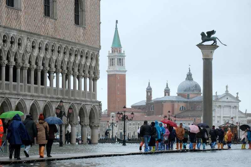 People walk on a catwalk in the flooded St.Mark's Square during a period of seasonal high water in Venice