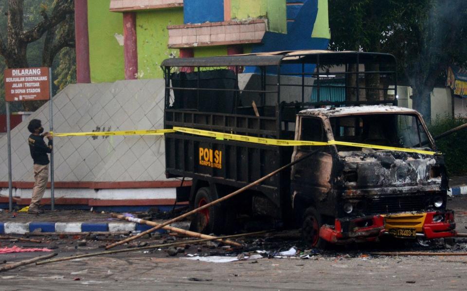 A policeman sets up a cordon next to a torched vehicle outside Kanjuruhan stadium in Malang - PUTRI/AFP