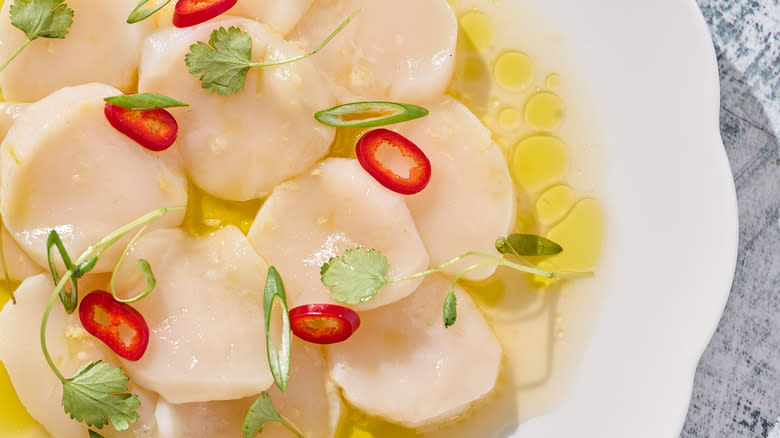 scallop crudo with yuzu, cilantro and chile on white plate