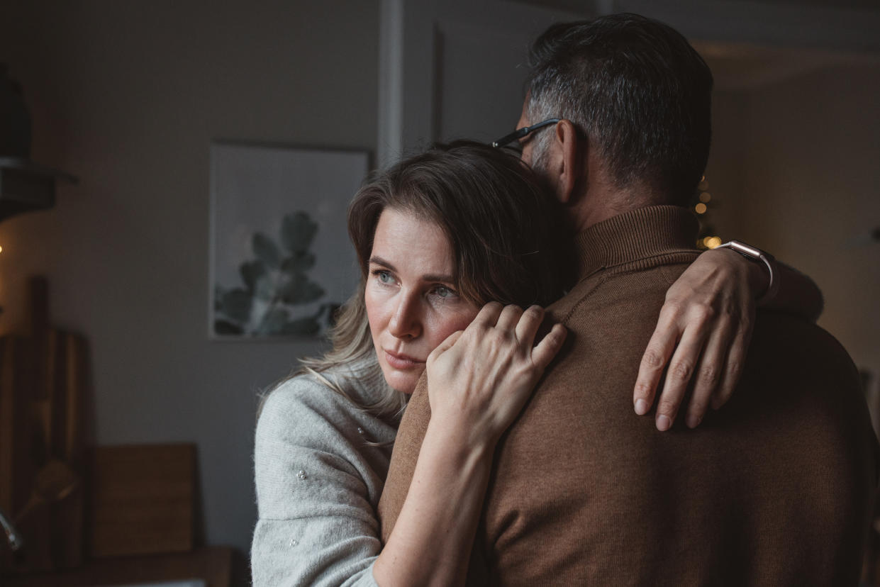 Mature couple for Christmas at home. They are standing in front of kitchen window and hugging.