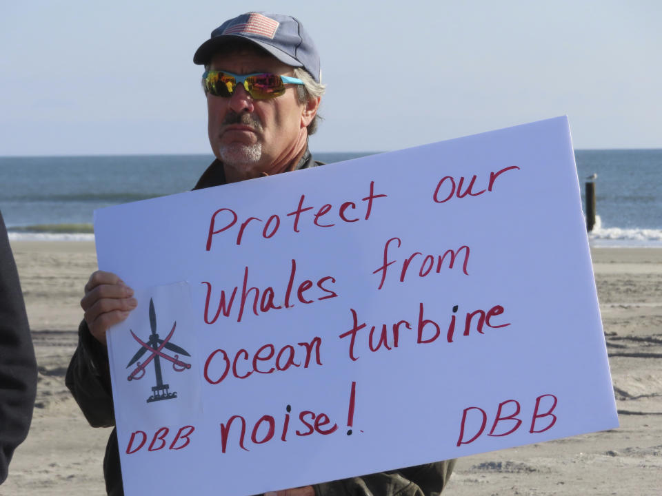 Tom Jones of the group Defend Brigantine Beach holds a sign at a press conference on the beach in Atlantic City, N.J., on Monday, Jan. 9, 2023, where a large dead whale was buried over the weekend. Several groups called for a federal investigation into the deaths of six whales that have washed ashore in New Jersey and New York over the past 33 days and whether the deaths were related to site preparation work for the offshore wind industry. (AP Photo/Wayne Parry)