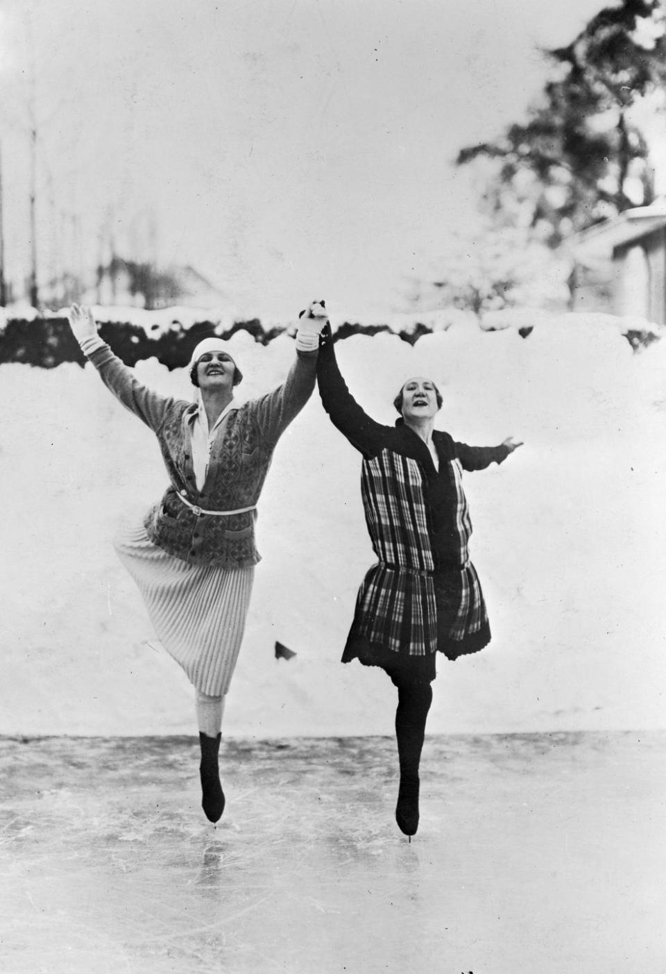 <p>Two women hold hands and kick their legs back as they strike a pose while ice skating in Berlin, Germany.</p>