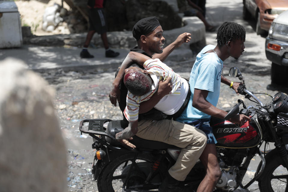 A police officer holds onto a man wounded during violent gang clashes, as they are driven away on the back of a moto-taxi, in the Carrefour-Feuilles district of Port-au-Prince, Haiti, Aug. 15, 2023. (AP Photo/Odelyn Joseph)