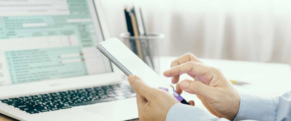 Close up of man's hands holding smartphone in front of laptop with tax forms up