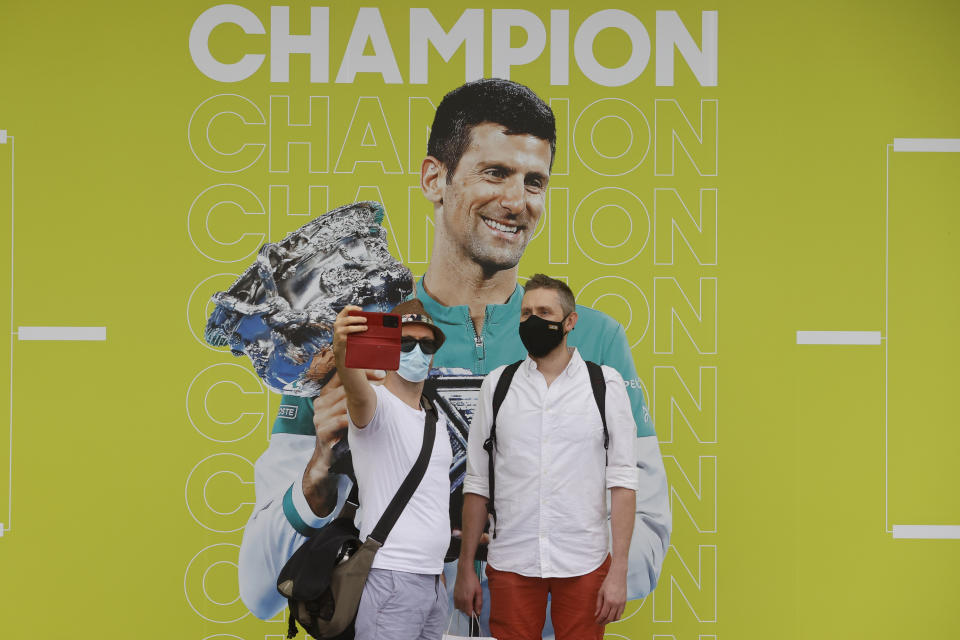 Fans take a selfie with a photo of defending champion Novak Djokovic of Serbia ahead of first round matches at the Australian Open tennis championships in Melbourne, Australia, Monday, Jan. 17, 2022. Djokovic was deported from Australia Sunday, Jan 16, after losing a bid to stay in the country to defend his Australian Open title despite not being vaccinated against COVID-19. (AP Photo/Hamish Blair)