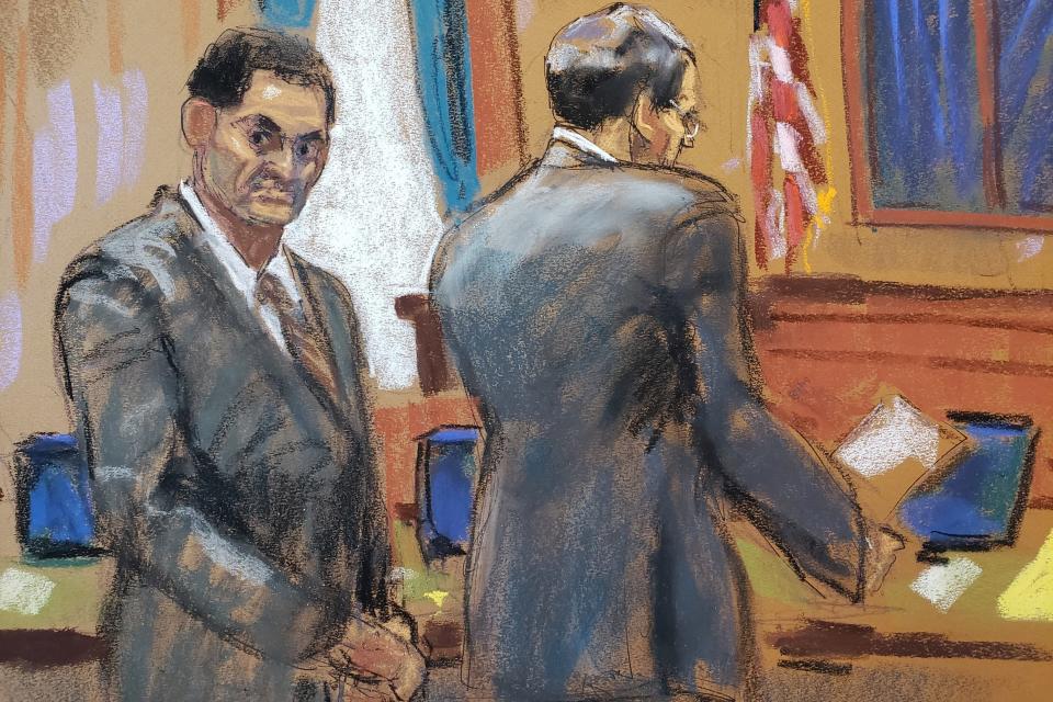 A courtroom sketch of Sam Bankman-Fried standing next to and looking behind his lawyer.