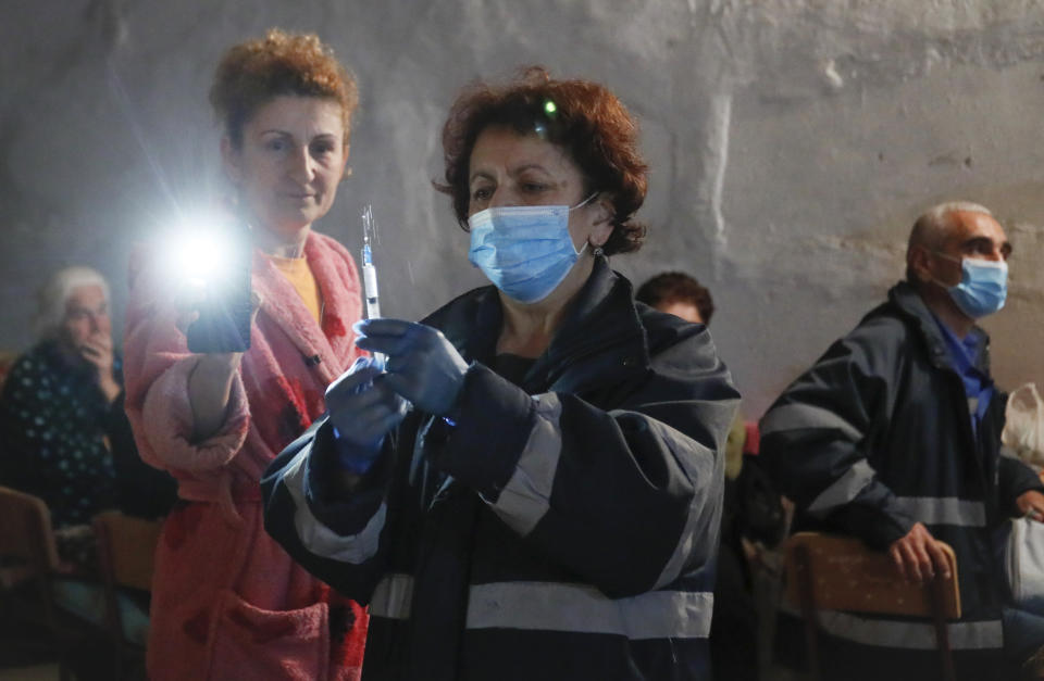 A woman uses her phone to provide light as a medical worker prepares a syringe of medication for a sick woman taking refuge in a bomb shelter in Stepanakert, the separatist region of Nagorno-Karabakh, Thursday, Oct. 22, 2020. Heavy fighting over Nagorno-Karabakh continued Thursday with Armenia and Azerbaijan trading blame for new attacks, hostilities that raised the threat of Turkey and Russia being drawn into the conflict. (AP Photo)