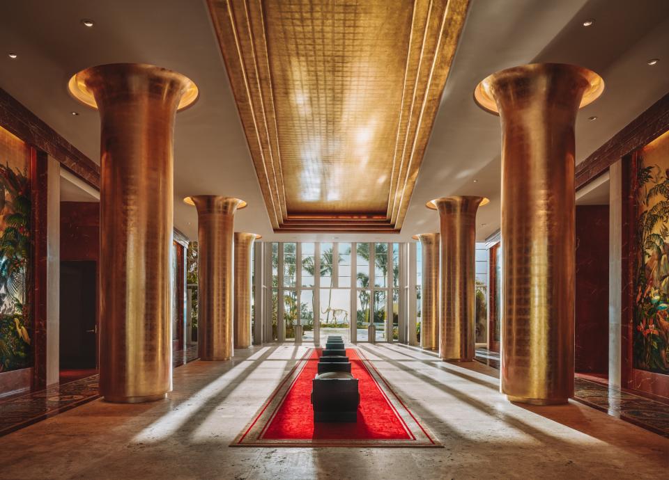 Nicknamed the Cathedral, the lobby of <a href="https://www.faena.com/" rel="nofollow noopener" target="_blank" data-ylk="slk:Faena Hotel Miami Beach;elm:context_link;itc:0;sec:content-canvas" class="link ">Faena Hotel Miami Beach</a> screams decadence and glamor. Rows of gilded columns line the double-height space and frame the view of Damien Hirst’s <em>Gone But Not Forgotten,</em> a sculpture of a gold wooly mammoth skeleton. Richly detailed floor-to-ceiling murals by Argentine Juan Gatti occupy the lobby’s walls and add to the opulent atmosphere.