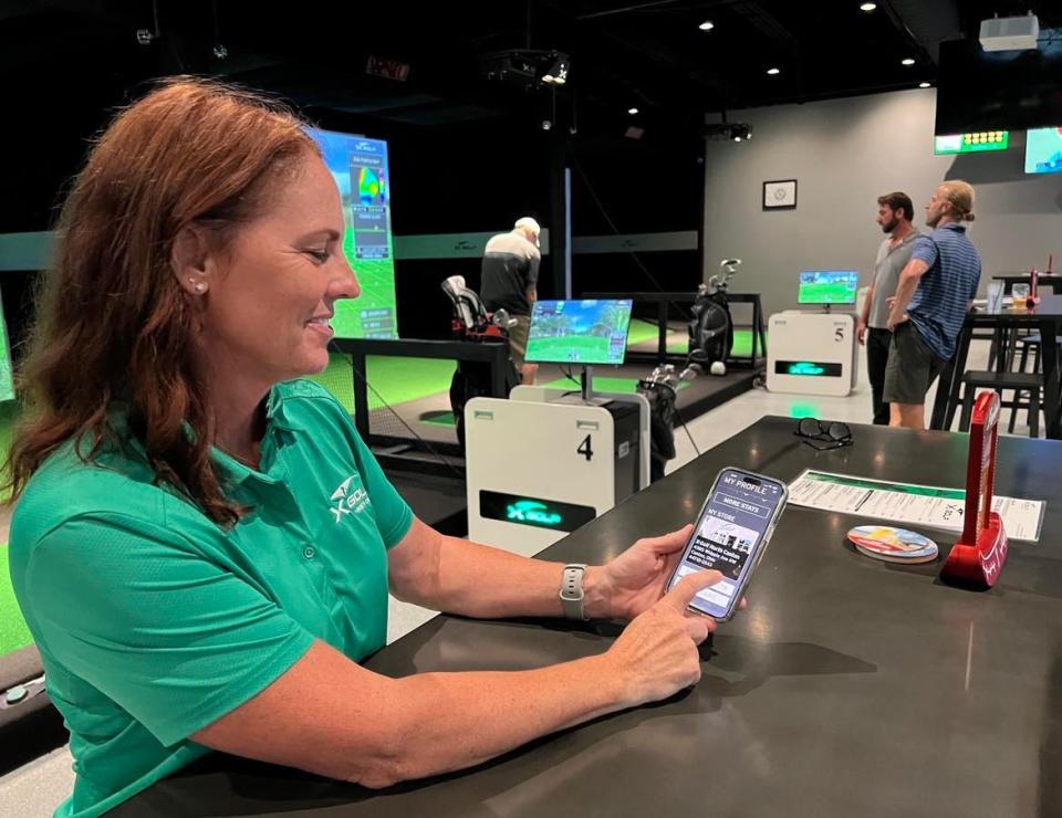 Jen Dillion, owner of X-Golf in Jackson Township, displays simulated golf features on her cellphone. X-Golf is one of several indoor golf venues in Stark County.