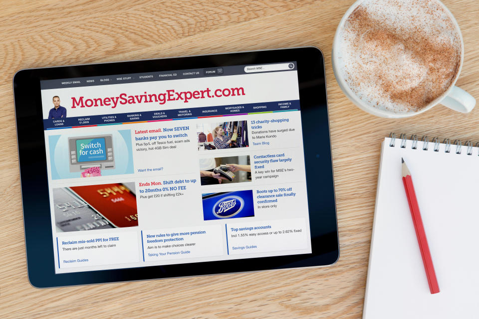 The MoneySavingExpert website features on an iPad tablet device which rests on a wooden table beside a notepad (Editorial use only).