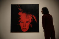 Una representante del A posa junto a un autorretrato de Andy Warhol de 1986 durante una presentación a la prensa de la exposición "Andy Warhol" en el Tate Modern de Londres, el martes 10 de marzo del 2020. La muestra estará abierta al público desde el 12 de marzo hasta el 6 de septiembre. (AP Foto/Matt Dunham)