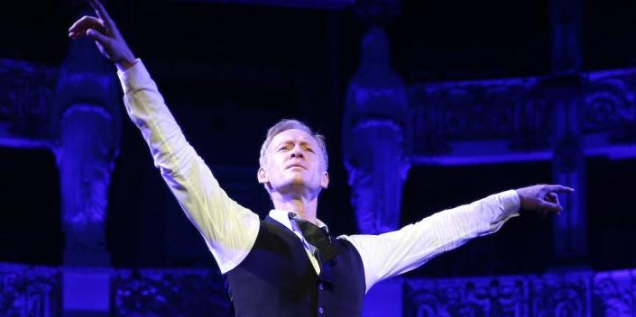 German ballet director Igor Zelensky pictured with arms raised on stage, with blue lighting behind him, in 2018.