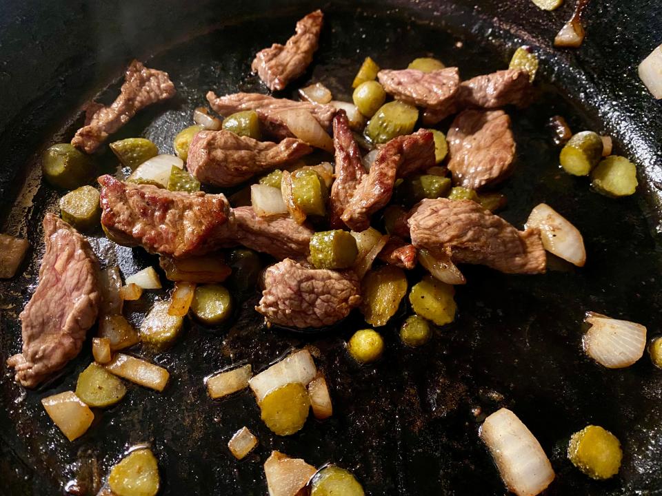 Beef, onion, and pickles in a pan.
