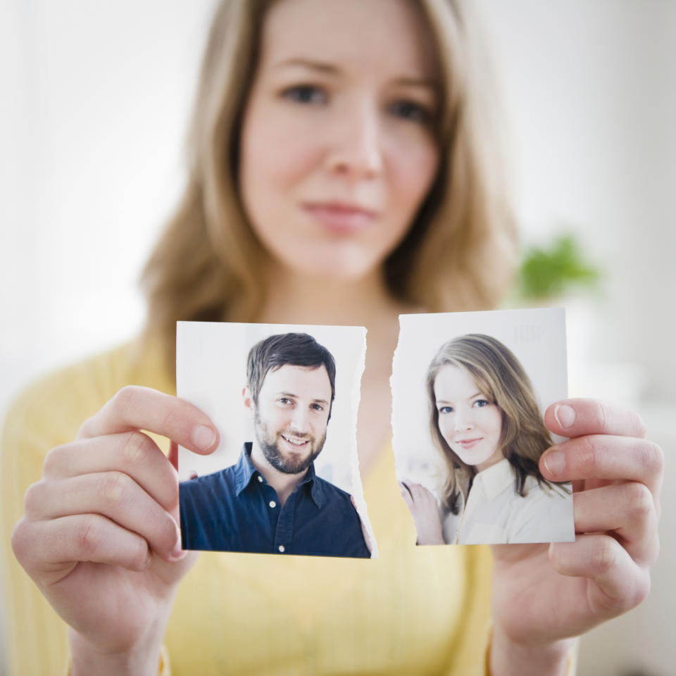 A woman holds a torn photograph of a man and a woman, both smiling, suggesting a breakup or separation