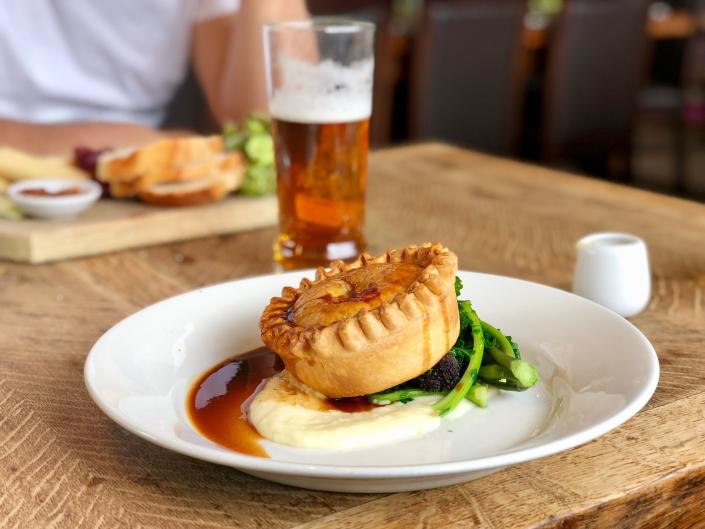 a small pie on a bed of mashed potatoes, green beans and gravy on a white plate on a table - dinner restaurant