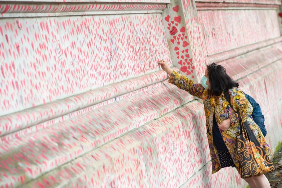 A woman writes a message on the Covid memorial wall in Westminster, London (Dominic Lipinski/PA) (PA Wire)