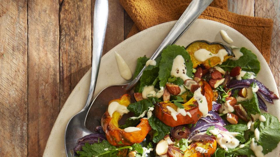 acorn squash salad with tahini vinaigrette on a cream colored oval plate with serving utensils