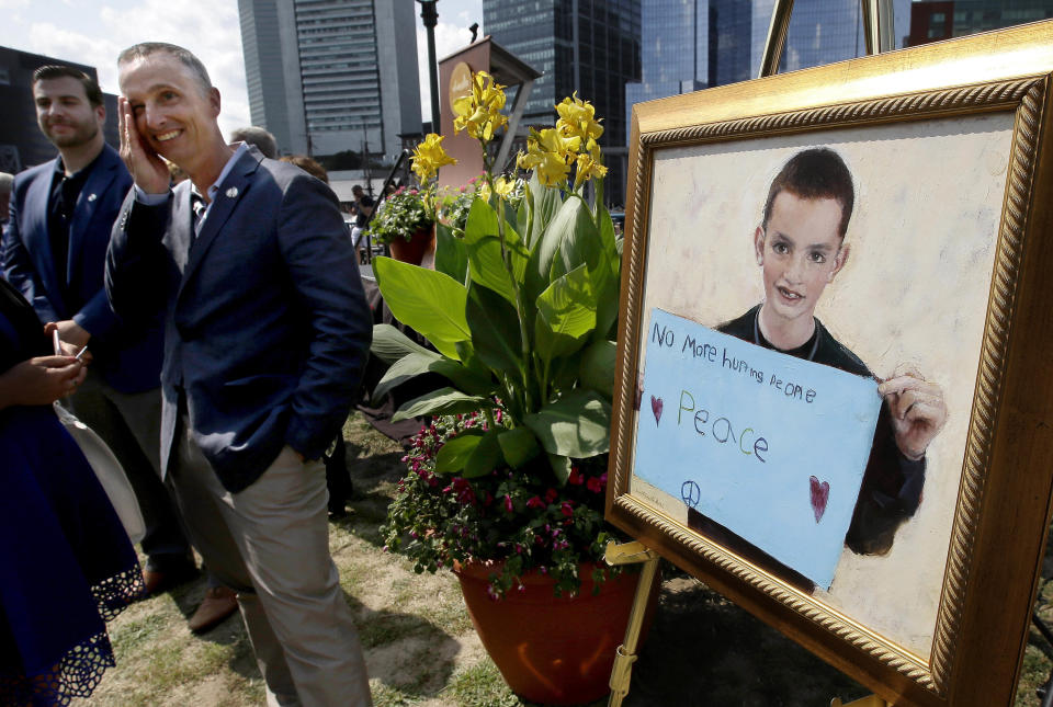 FILE - Bill Richard, second from left, stands beside a painting of his son Martin Richard, the youngest person killed in the Boston Marathon bombing in 2013, at the conclusion of groundbreaking ceremonies Aug. 16, 2017, for a Boston park named in Martin's honor. The painting pays tribute to a photograph that shows Martin holding a sign with the words "No more hurting people. Peace." (AP Photo/Steven Senne, File)