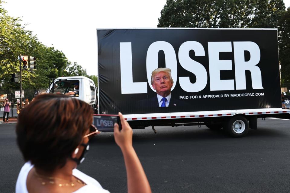 Joy Jackson photographs a passing truck bearing an image of then-President Donald Trump superimposed on a block of letters reading “LOSER” on August 2020 in Washington, D.C. The former president has officially announced his candidacy for the 2024 presidency. (Photo by Michael M. Santiago/Getty Images)