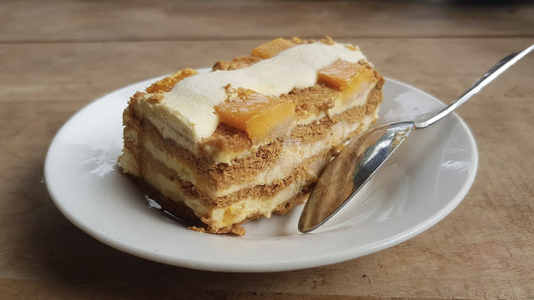 Slice of mango float cake on white plate with spoon