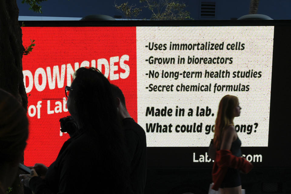 People stand outside the entrance to a pop-up tasting event for "lab-grown" meat produced by Upside Foods, as a protest truck parked out front displays a message advocating against cultivated meat, Thursday, June 27, 2024, in Miami. As Florida's ban on lab-grown meat is set to go into effect next week, one manufacturer hosted a tasting party, serving up cultivated chicken tostadas to dozens of attendees on a rooftop in Miami's Wynwood neighborhood. (AP Photo/Rebecca Blackwell)