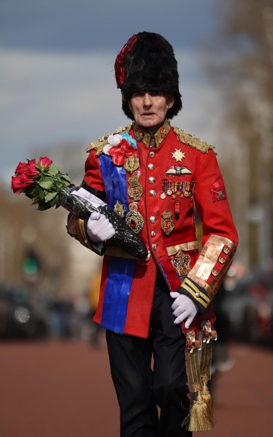 An elderly member of the public wearing an outfit in the style of a vintage ceremonial military uniform carries a floral tribute outside Buckingham Palace  - Dan Kitwood/ Getty Images 