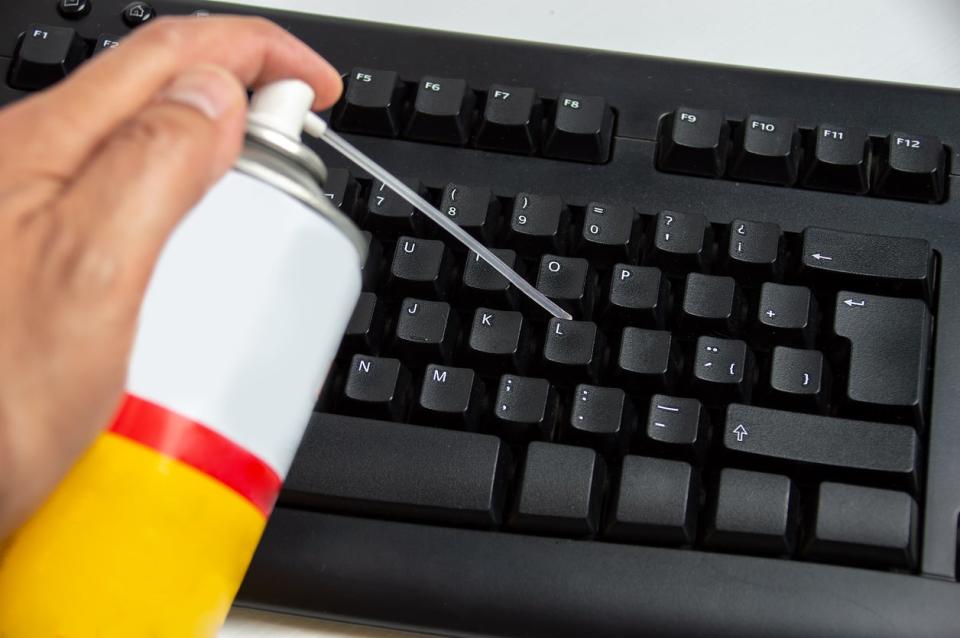 Using can of compressed air to clean a black computer keyboard