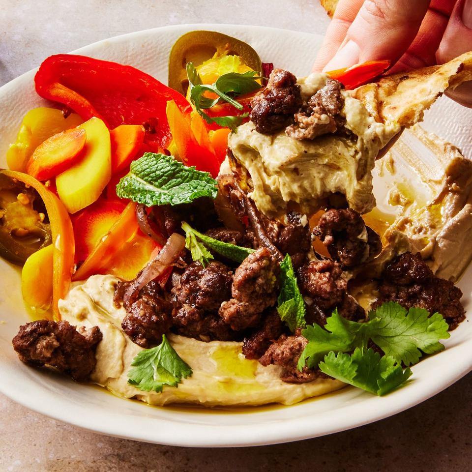 hummus bowl topped with spiced lamb, homemade pickled vegetables, and herbs