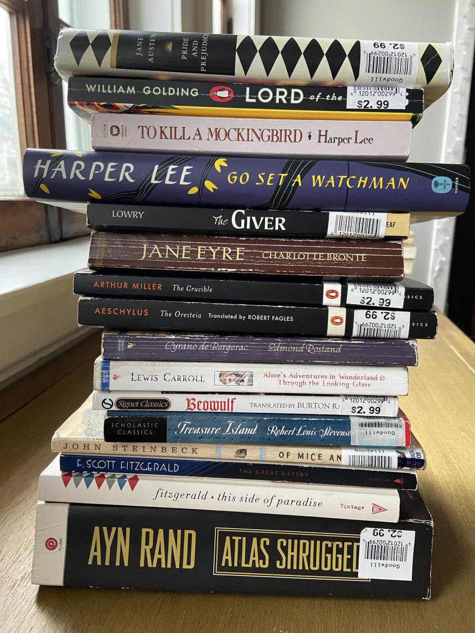 photo of a stack of books including titles "Atlas Shrugged," "This Side of Paradise," "Of Mice and Men," "Treasure Island," and "Beowulf"