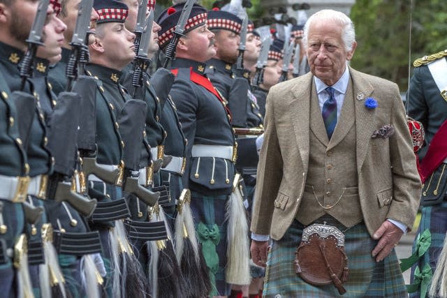 The King wearing a kilt and sporran inspects Royal Regiment of Scotland soldiers at the gates of Balmoral