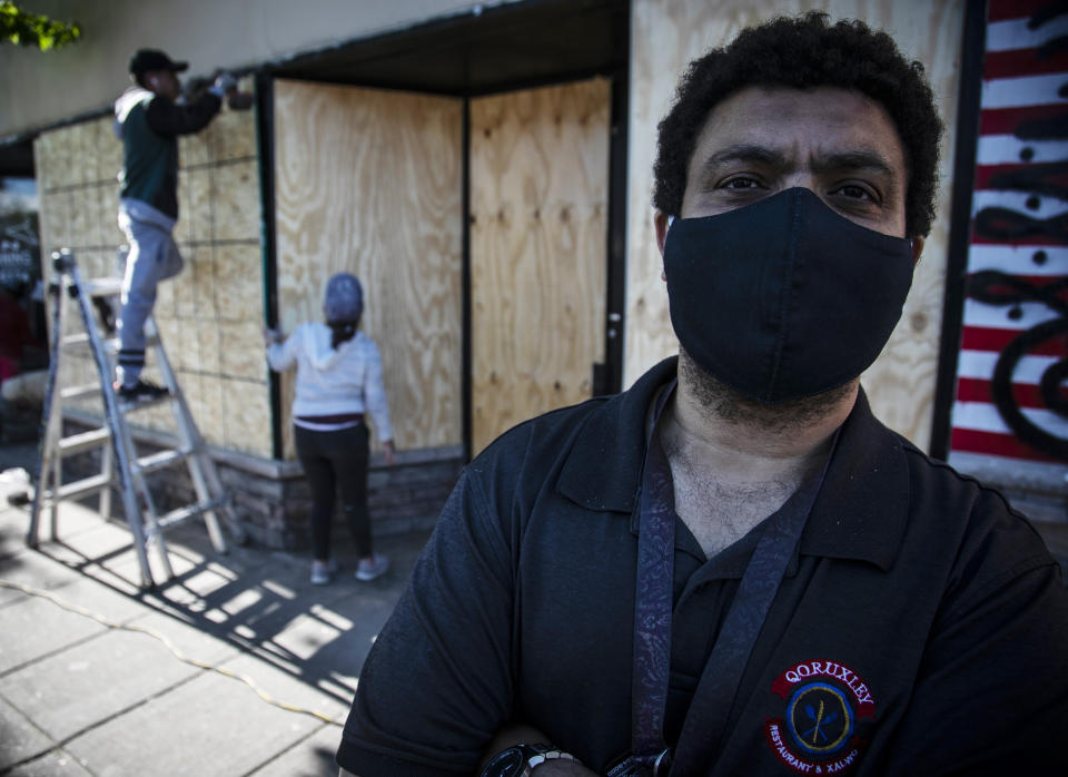 El inmigrante somalí Ahmed Faid posa frente a su negocio en la calle Lake Street de Minneapolis mientras obreros cubren con tablones el frente de su negocio el 30 de mayo del 2020. (AP Photo/Bebeto Matthews)