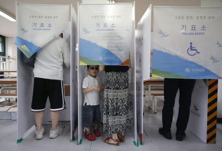 A boy waits for his mother as she marks her ballot in a voting booth for the local elections at a polling station in Seoul June 4, 2014. REUTERS/Kim Hong-Ji