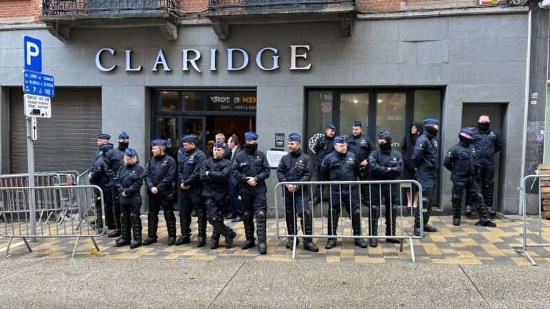 A large gaggle of blue-clad police officers barricade the entrance to the NatCon Brussels 2 conference at the gray-walled Claridge event space in Belgium.