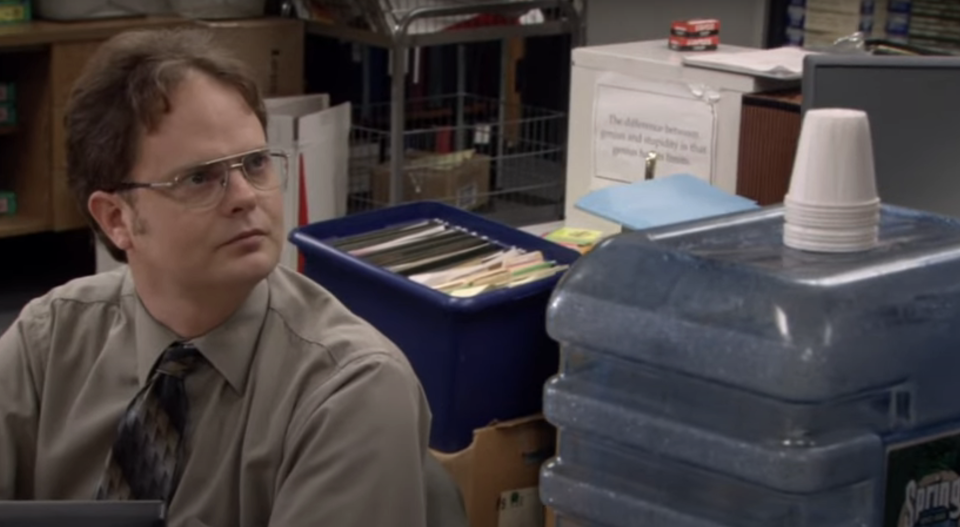 Character Dwight from "The Office" sits at a desk, looking to the side with a serious expression