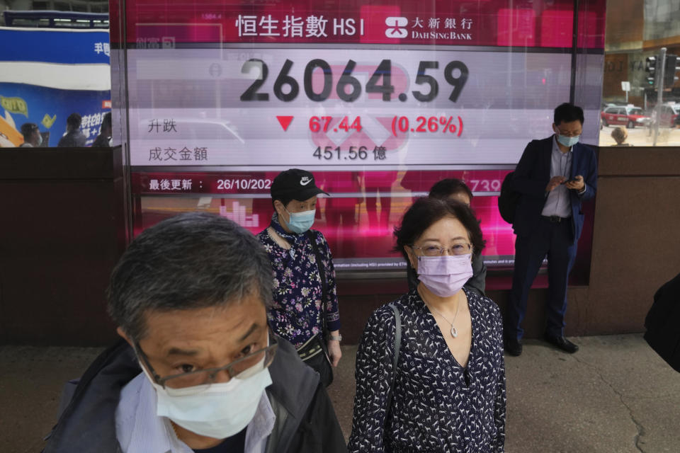 People wearing face masks walk past a bank's electronic board showing the Hong Kong share index in Hong Kong, Tuesday, Oct. 26, 2021. Asian shares were mostly higher Tuesday after another rally to a record high on Wall Street. (AP Photo/Kin Cheung)