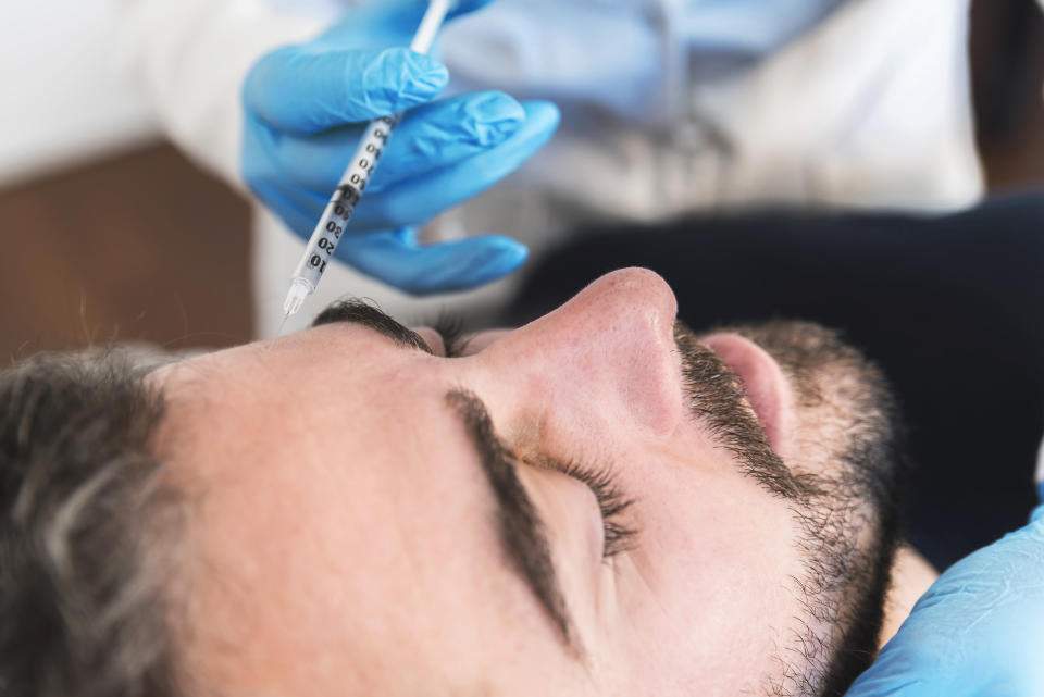 Close up of man at clinic receiving injection fillers on forehead.