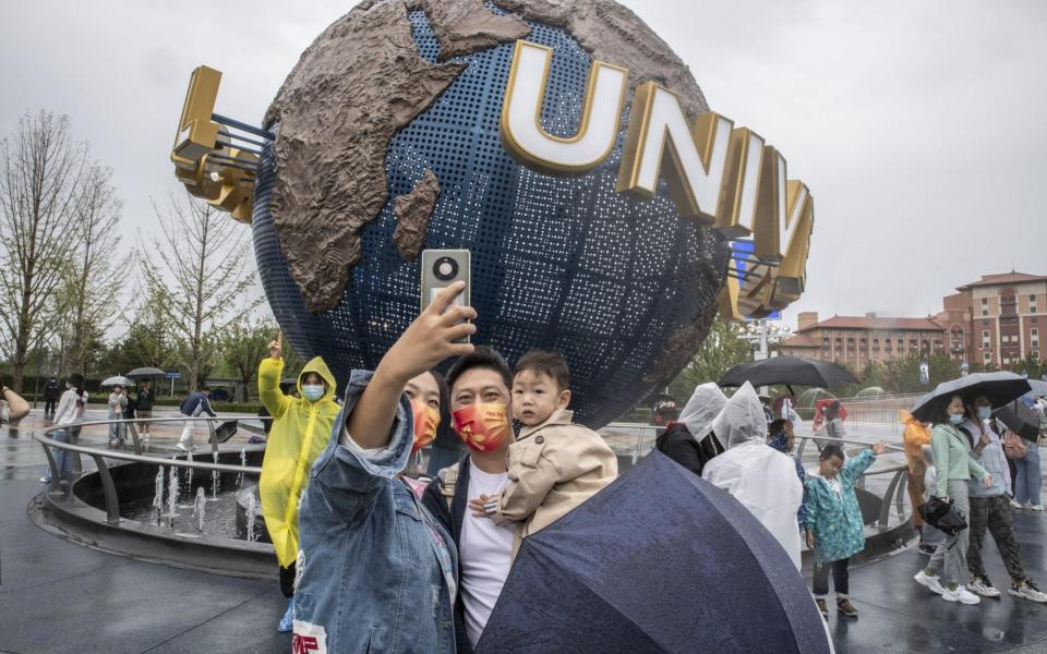 A family wearing face masks take selfies at the entrance of the Universal Studios Beijing theme park on 20 September 2021 - Gilles Sabrie/Bloomberg