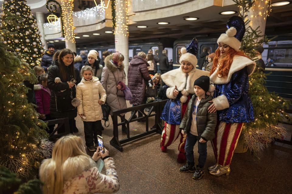 Women dressed in costumes pose with a boy for a photograph at the subway station "University" decorated for Christmas and New Year in Kharkiv, Ukraine, Saturday, Dec. 31, 2022. (AP Photo/Evgeniy Maloletka)