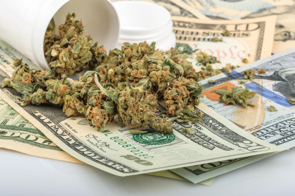 A tipped-over bottle of cannabis buds lying atop a messy pile of cash bills.