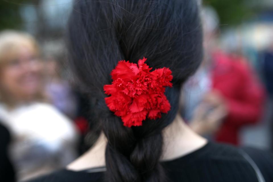A woman wears a red carnation in her hair as she walks with others celebrating the 40th anniversary of the 25th April revolution that restore the democracy in Portugal in 1974, on Friday April 25, 2014. Euphoria gripped Portugal during the 1974 Carnation Revolution, when junior army officers swept away a four-decade dictatorship. The almost bloodless coup brought what for the Portuguese were novelties, the right to vote, universal health care, public education, old-age pensions and labor rights. (AP Photo/Francisco Seco)