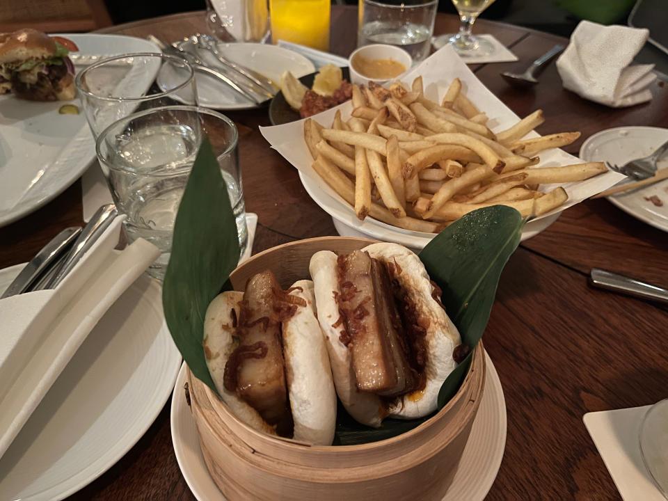 The food at Spago — pork bao, french fries, a burger, and wings visible.