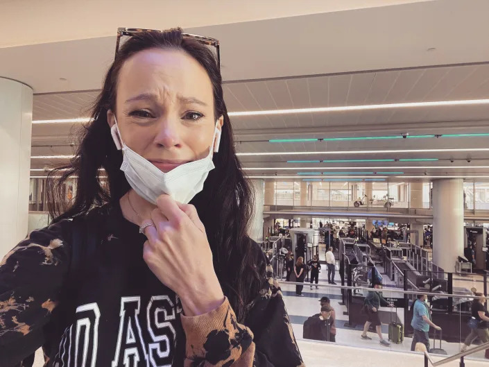 A woman stands at an airport in tears.