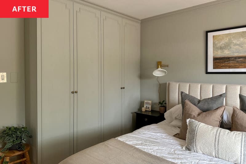 Primary bedroom after renovation: Bed with quilted gray headboard, sliding glass doors letting in light with open pale neutral curtains, pale nuted green walls, framed painting over bed, new built in floor to ceiling closet, small stool with plant on it. Bed has bedding in grays and browns, lots of pillows